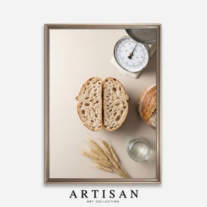 Puede incluir: Naturaleza muerta enmarcada con una hogaza de pan cortada por la mitad, una hogaza entera, una balanza vintage, un vaso de agua y espigas de trigo. La imagen tiene una paleta de colores neutros con el texto "ARTISAN ART COLLECTION" en la parte inferior.