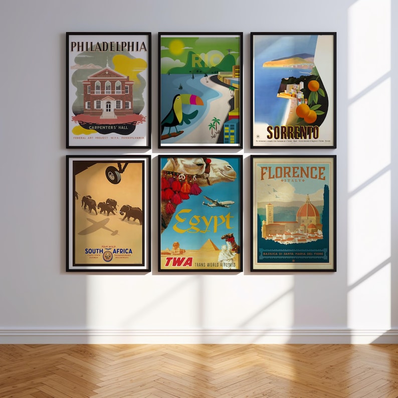 May include: A wall gallery of vintage travel posters featuring destinations like Philadelphia, Rio, Sorrento, Egypt, Florence, and South Africa. The posters are framed in black and feature colorful illustrations and typography.