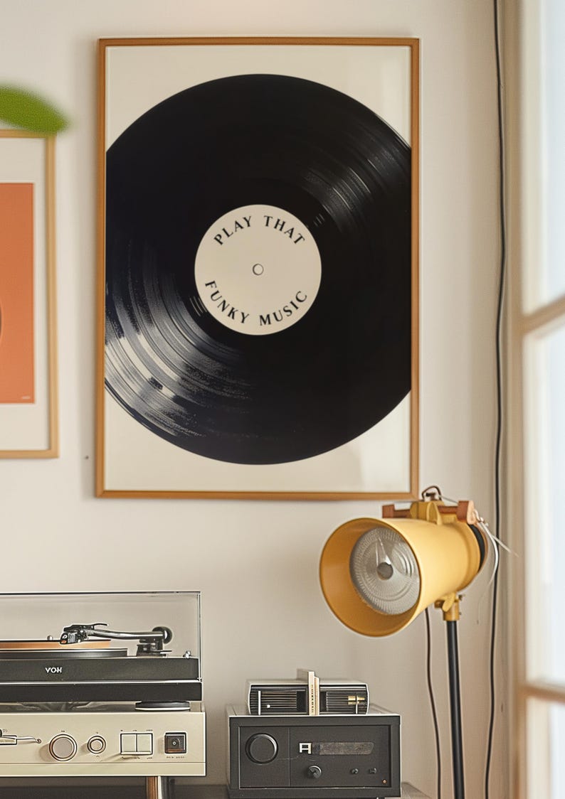 May include: A framed print of a black vinyl record with the text "Play That Funky Music" in white. The print is hanging on a white wall next to a record player and a yellow lamp.