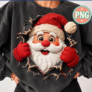 May include: A charcoal gray sweatshirt featuring a central graphic of a Santa Claus face emerging from a torn fabric effect. Santa wears a red hat with a white pom-pom and red mittens. The graphic includes a circular logo with the text PNG.