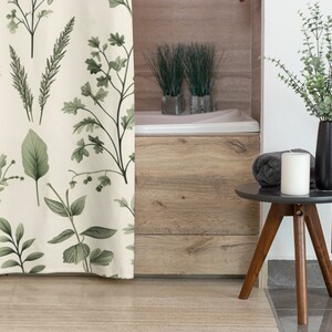 Puede incluir: Una cortina de ducha blanca con un patr&oacute;n de hojas verdes. La cortina est&aacute; colgada en un ba&ntilde;o con una ba&ntilde;era de madera y una peque&ntilde;a mesa auxiliar con una vela y un jarr&oacute;n de vegetaci&oacute;n.