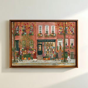 May include: A framed painting of a red brick building with an Independent Book Shop storefront. The scene features people walking on the sidewalk, autumn trees with orange leaves, and pumpkins placed near the entrance and windows.