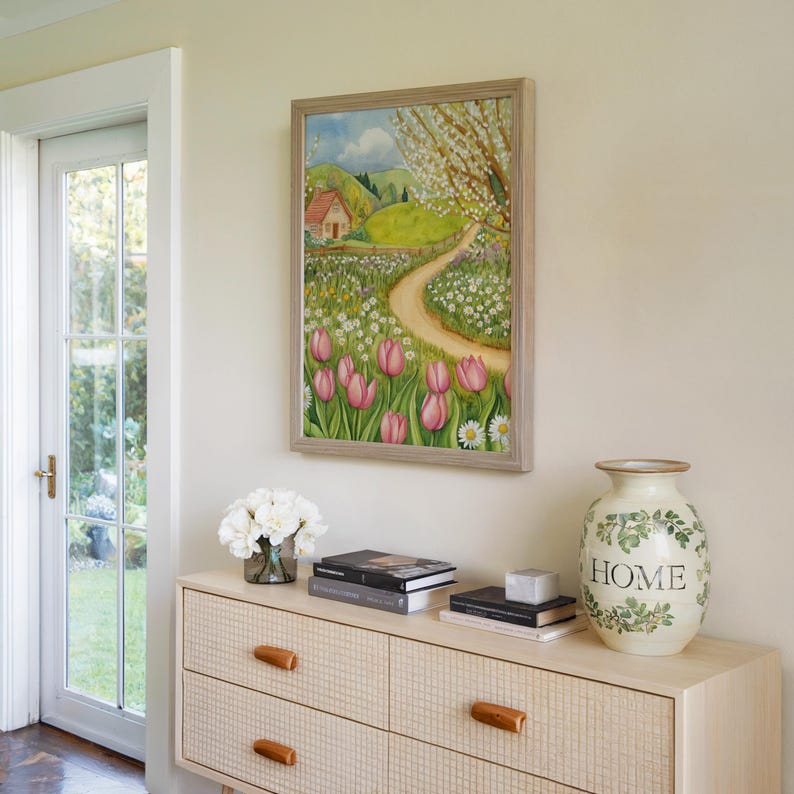 Watercolor illustration of a spring cottage meadow with pink tulips, white daisies, a winding path, and a small countryside house under blooming trees in cottagecore style. Spring landscape farmhouse decor cozy cottage printable wall art cottage decor cozy home decor spring flowers digital download pink tulip wall art tulip wall decor.