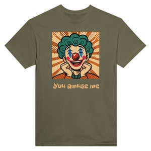 Op de afbeelding: Olijfgroen t-shirt met een cartoon clown ontwerp. De clown heeft turquoise haar, een rode neus en een lachend gezicht. Het ontwerp staat tegen een retro achtergrond, met de tekst "You amuse me" eronder.