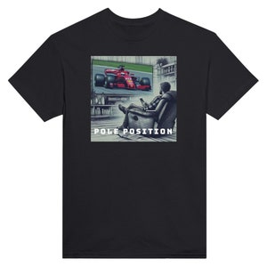 Puede incluir: Una camiseta negra con un gráfico de una persona viendo un coche de carreras rojo en una pantalla de televisión. El texto "POLE POSITION" está impreso debajo del gráfico.