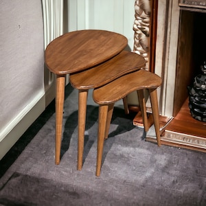 Puede incluir: Tres mesas nido de madera con una forma curva única y un acabado marrón oscuro. Las mesas están dispuestas en forma escalonada, con la mesa más grande en la parte inferior y la mesa más pequeña en la parte superior.