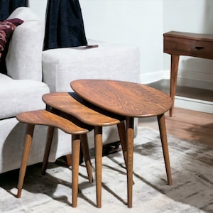 May include: Three wooden nesting tables with a unique, organic shape. The tables are made of dark brown wood and have a natural finish. The tables are arranged in a staggered formation, with the largest table in the back and the smallest table in the front.
