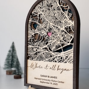 May include: A wooden map art piece with a layered design, featuring a city map with a pink heart marking a location. The text "Where it all began" is displayed, along with names and a date. The frame is dark brown.