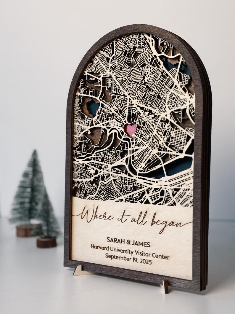 May include: A wooden map art piece with a layered design, featuring a city map with a pink heart marking a location. The text "Where it all began" is displayed, along with names and a date. The frame is dark brown.
