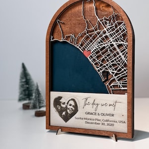 May include: Wooden map art piece with a laser-cut city map, a heart-shaped photo, and the text "The day we met." The map features a red heart marking a location. The piece includes the names Grace & Oliver and the date December 30, 2020.