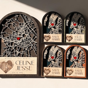 May include: A collection of personalized wooden map art pieces. Each piece features a city map with a red heart marking a location, and includes names and a date. The pieces are in various wood tones and sizes.