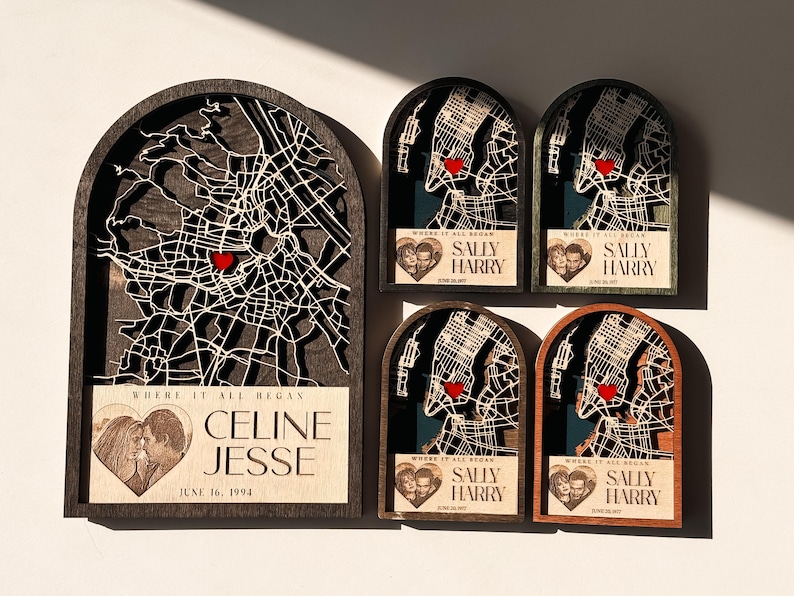 May include: A collection of personalized wooden map art pieces. Each piece features a city map with a red heart marking a location, and includes names and a date. The pieces are in various wood tones and sizes.