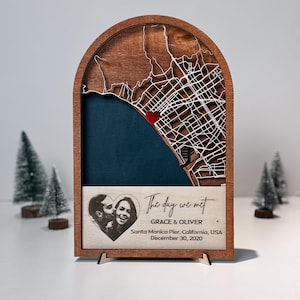 May include: A wooden map art piece with a laser-cut city map, a red heart, and a blue background. The text "The day we met" is above a photo of a couple and the names GRACE & OLIVER. The date and location are also included.