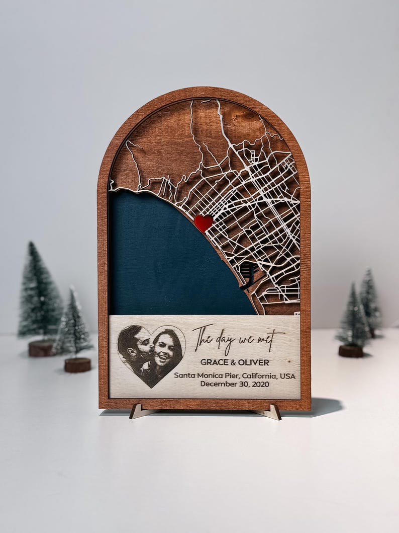 May include: A wooden map art piece with a laser-cut city map, a red heart, and a blue background. The text "The day we met" is above a photo of a couple and the names GRACE & OLIVER. The date and location are also included.