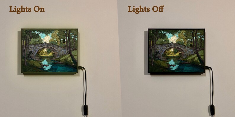 May include: A framed landscape artwork showing a stone bridge over a river, surrounded by trees. The image is displayed with the lights on and off, showing the illuminated and non-illuminated versions. The frame is dark.