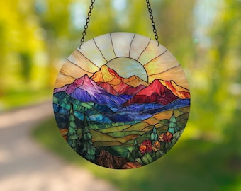 May include: A stained glass suncatcher depicting a colorful mountain landscape with a sunrise over the peaks. The suncatcher is round and features a variety of colors, including blue, green, yellow, orange, and red.
