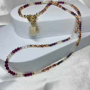 May include: A multi-strand necklace with a gold clasp and a small white stone pendant. The necklace is made of small beads in shades of red, orange, white, and gold.