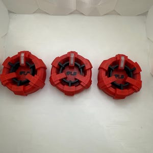 Puede incluir: Tres tapas de pl&aacute;stico rojo con detalles negros y las letras "FJ" impresas en ellas. Las tapas tienen un dise&ntilde;o en relieve y una peque&ntilde;a luz blanca en la parte superior.