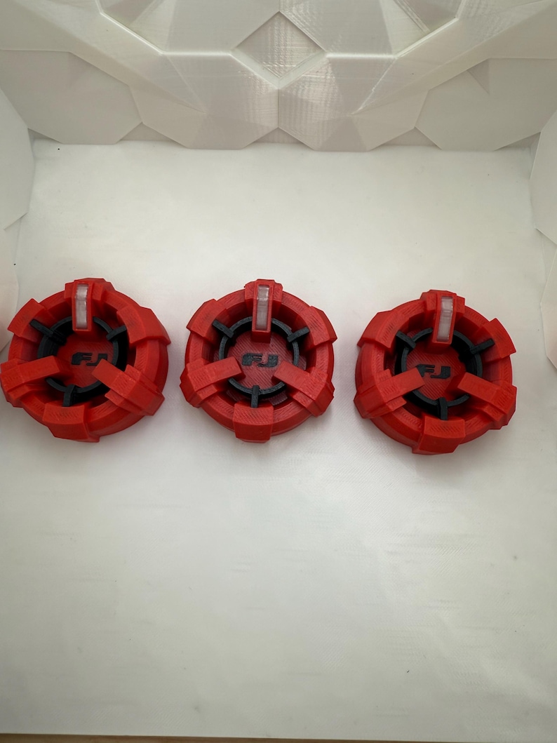 Puede incluir: Tres tapas de pl&aacute;stico rojo con detalles negros y las letras "FJ" impresas en ellas. Las tapas tienen un dise&ntilde;o en relieve y una peque&ntilde;a luz blanca en la parte superior.