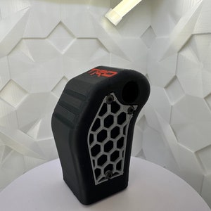 May include: A black 3D printed gear shift knob with a silver honeycomb pattern and the word "TRO" in red lettering.