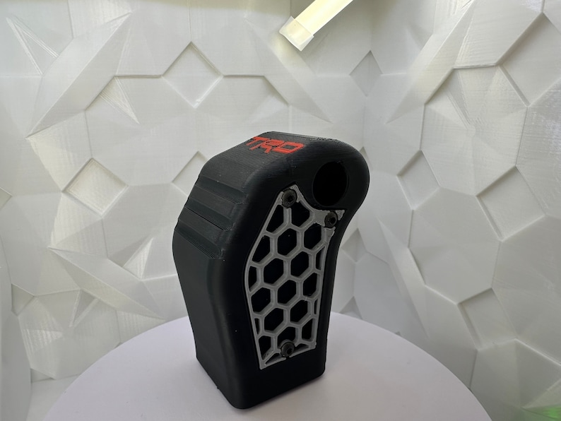 May include: A black 3D printed gear shift knob with a silver honeycomb pattern and the word "TRO" in red lettering.