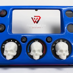Puede incluir: Un panel azul del salpicadero del coche con mandos blancos en forma de calavera para el control de la temperatura. El panel tiene botones negros y el texto "PRINT WERX DESIGNS". Los mandos están sobre fondos circulares negros con indicadores de temperatura.