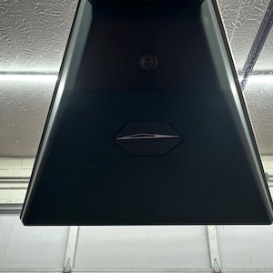 Puede incluir: Una lámpara de techo triangular negra con un pequeño sensor redondo en el centro y una forma rectangular plateada en el medio.