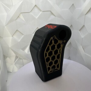 May include: Black gear shift knob with a gold honeycomb pattern and the word "TRO" in red lettering.
