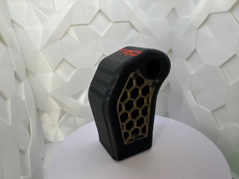 May include: Black gear shift knob with a gold honeycomb pattern and the word "TRO" in red lettering.