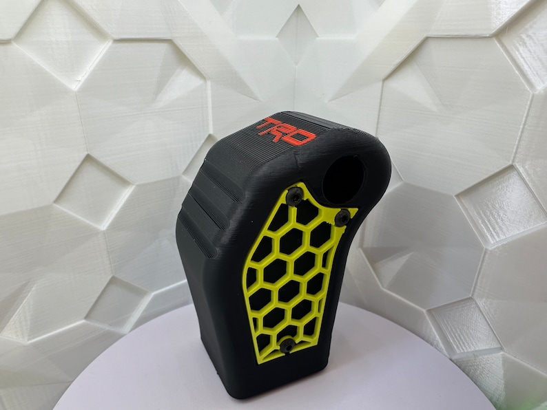 May include: Black gear shift knob with a yellow honeycomb pattern and the word "TRD" in red lettering.