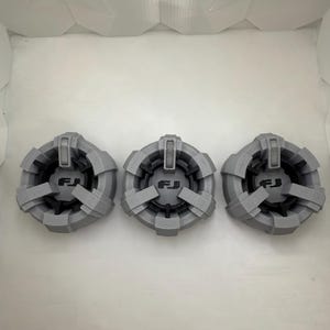 Puede incluir: Tres tapacubos de pl&aacute;stico gris con un logotipo "FJ" negro en el centro.
