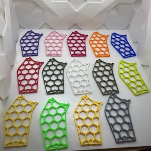 May include: A collection of 15 plastic honeycomb-shaped pieces in various colors, including red, purple, pink, orange, yellow, green, white, and gray. The pieces are arranged in rows on a white surface.