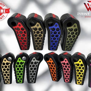 Op de afbeelding: Een verzameling zwarte accessoires met honingraatontwerpen in verschillende kleuren. De accessoires hebben een gebogen vorm en zijn in rijen gerangschikt. De kleuren zijn onder meer rood, goud, blauw, groen, wit, zilver, oranje, roze, geel en paars.