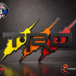 Pode incluir: Emblema TRD preto, amarelo, laranja e vermelho com design de raio. Fabricado nos EUA e com garantia vitalícia. O logotipo Print Werx Designs está no canto inferior direito.