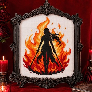 Può includere: Ricamo a punto croce di una silhouette nera di una figura con due spade, ambientata su uno sfondo di fiamme nei toni dell'arancione e del rosso. L'opera è incorniciata in una cornice nera decorativa, con candele e rose sullo sfondo.