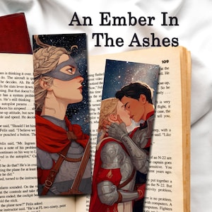 Puede incluir: Un libro abierto con dos marcadores ilustrados. Los marcadores presentan a una mujer con máscara y una pareja besándose. El título del libro, "An Ember In The Ashes", se muestra en la parte superior. Un libro cerrado descansa a la izquierda.