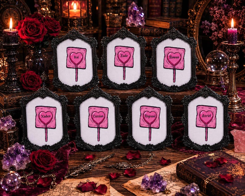 May include: Eight framed artworks with black ornate frames. Each frame holds a pink heart-shaped design on a white background, resembling a lollipop, with a name in the center. The names are Kai, Zade, Rowan, Xaden, Cassian, Rhysand, and Azriel.