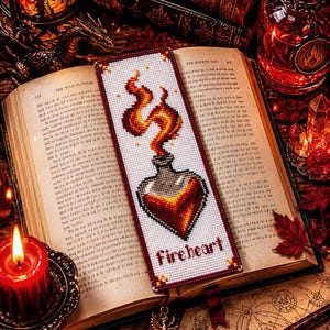 May include: A rectangular bookmark featuring a cross-stitch design of a heart-shaped glass bottle emitting orange and yellow flames. The word Fireheart is stitched in dark red letters at the bottom of the white fabric background.