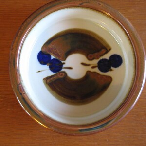 May include: Ceramic bowl with a cream-colored interior and a brown and blue abstract design. The rim is a darker brown. The bowl is likely for serving food or as a decorative piece.
