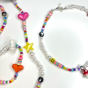 Puede incluir: Una colección de coloridas cadenas para gafas con cuentas. Las cadenas presentan varios dijes, incluyendo corazones, estrellas, caras sonrientes y símbolos de yin-yang. Las cuentas son de una variedad de colores, incluyendo rosa, amarillo, naranja y azul.