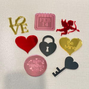 May include: Assortment of Valentine's Day themed acrylic mirror tiles. The tiles feature various designs including a heart with the words "Be Mine", a calendar with the date "Feb 14", a padlock, a key, a cupid, a heart, and a circle with the words "Happy Valentine's Day".