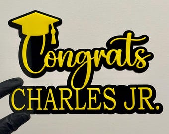 May include: Yellow and black graduation sign with the text "Congrats Charles JR." and a graduation cap.
