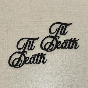 May include: Two black cursive cutouts that read "Til Death" are displayed on a light gray surface. The words are in a decorative script font, with the letters connected. The image is well-lit and the focus is sharp.