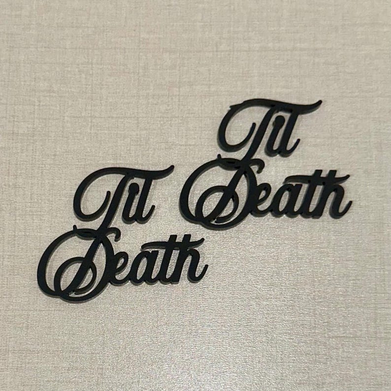 May include: Two black cursive cutouts that read "Til Death" are displayed on a light gray surface. The words are in a decorative script font, with the letters connected. The image is well-lit and the focus is sharp.