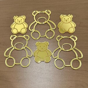 May include: Five gold mirror acrylic bear outlines of varying sizes. The bears are all facing forward with their arms outstretched.