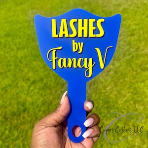 May include: Blue plastic hand mirror with a yellow inscription that reads "Lashes by Fancy V".