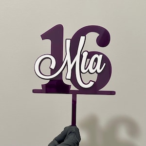 May include: Purple acrylic cake topper with the number 16 and the name Mia in white lettering.