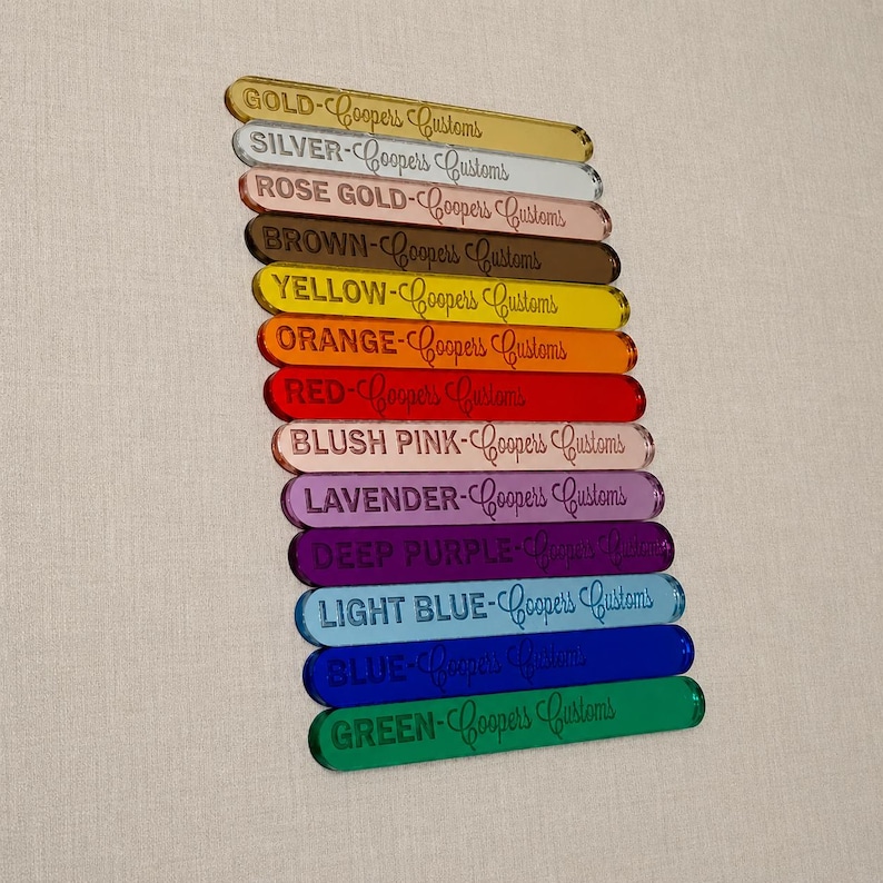 Op de afbeelding: Een stapel van twaalf rechthoekige acryl kleurstalen, elk gegraveerd met de kleurnaam en de tekst Coopers Customs. De kleuren zijn goud, zilver, ros&eacute;goud, bruin, geel, oranje, rood, oudroze, lavendel, donkerpaars, lichtblauw, blauw en groen.