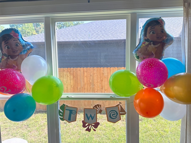 May include: A colourful display of balloons in shades of pink, blue, green, orange, white, and yellow. Two foil balloons depict a cartoon character. A banner spells "TWO" with tropical designs, ideal for a birthday party.