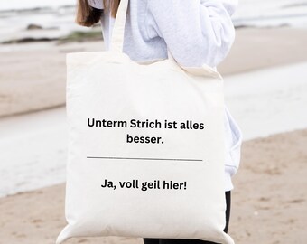 May include: White tote bag with black text that reads "Unterm Strich ist alles besser. Ja, voll geil hier!"